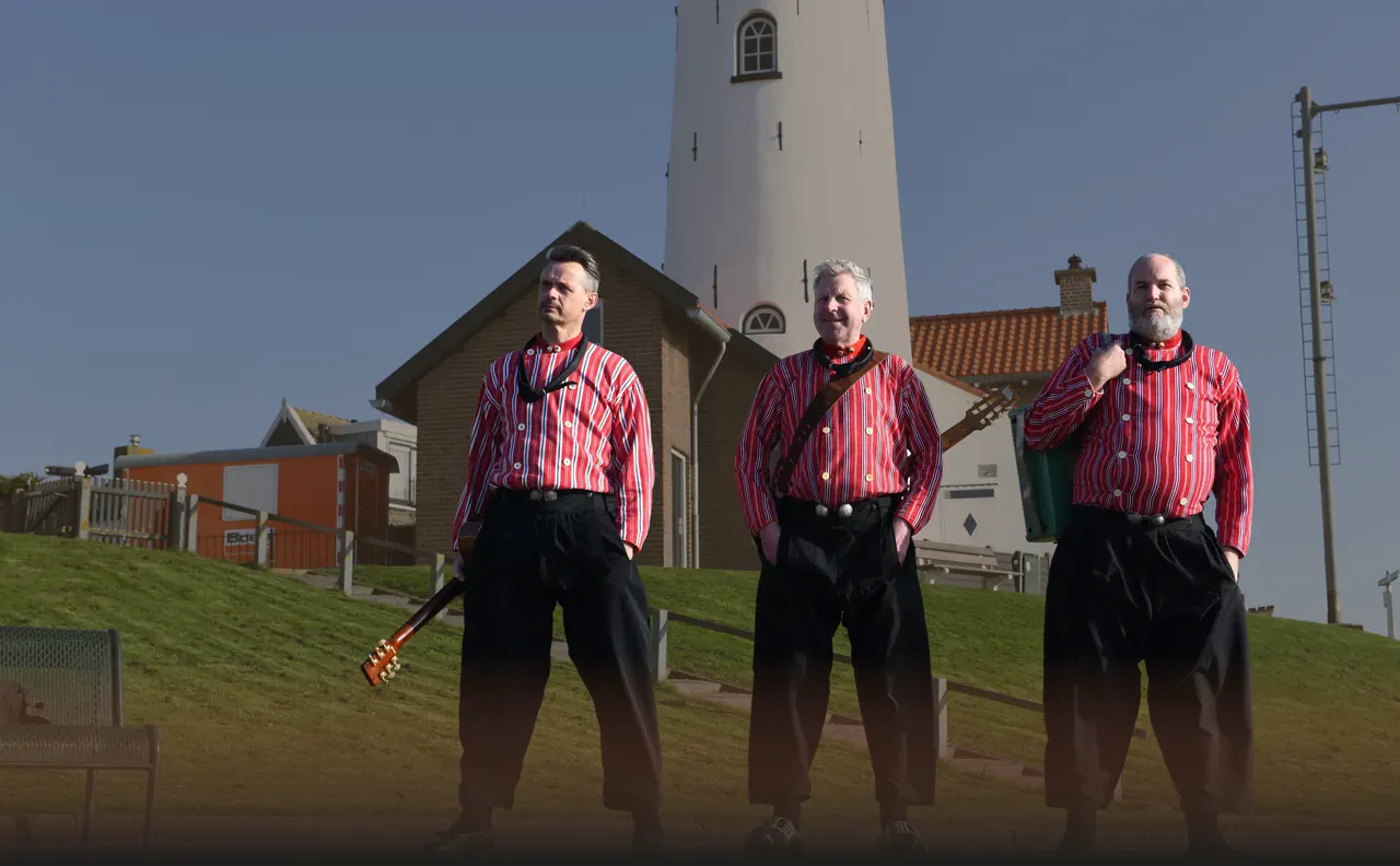 De drie muzikanten van Leuster in Urker dracht op de dijk bij de vuurtoren van Urk.